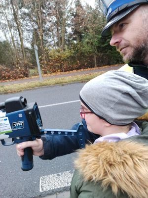 Na zdjęciu widoczny policjant mierzący prędkość, obok dziecko.