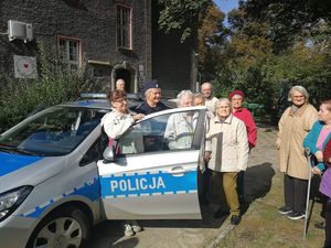 Na zdjęciu radiowóz, policjantka i seniorzy.