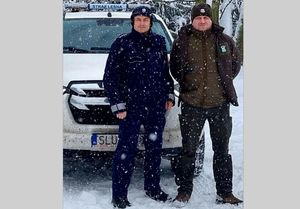 Na zdjęciu widoczny policjant, strażnik leśny na tle samochodu straży leśnej.