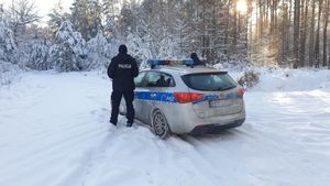 Na zdjęciu ośnieżony las, radiowóz oraz policjanci.