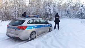 Na zdjęciu radiowóz, ośnieżony las oraz policjanci.