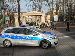 Na zdjęciu widoczny radiowóz blokujący drogę, oraz przemarsz Orszaku Trzech Króli, wychodzący z kościoła wierni ubrani w papierowe korony.