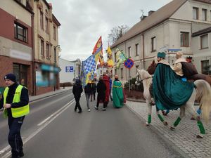 Na zdjęciu widoczny policjant regulujący ruchem na drodze, w tle widoczny orszak Trzech Króli, przebrani za monarchów mężczyźni jadący na koniach, w tle idący wierni.