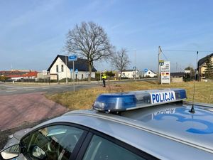 Na zdjęciu widoczny radiowóz oraz policjant stojący przy drodze i mierzący prędkość.