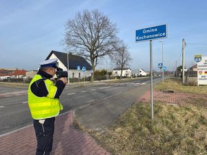 Na zdjęciu widoczny policjant stojący przy drodze i mierzący prędkość.