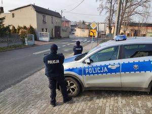 Na zdjęciu widoczni policjanci stojący przy radiowozie i obserwujący drogę.