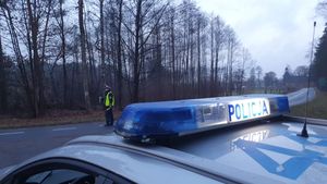 Na zdjęciu widoczny radiowóz, na drodze stojący policjant który bada kierującego samochodem  na zawartość  alkoholu  w wydychanym powietrzu.