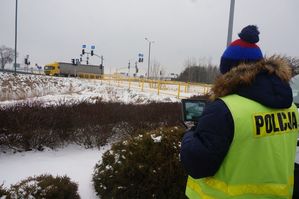 Na zdjęciu policjant stojący z monitorem w dłoniach.