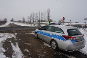 na zdjęciu widoczny radiowóz stojący przy drodze, obok niego stoi policjant.