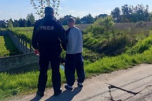 na zdjęciu widoczny umundurowany policjant obok sprawca rozboju z rękami do przodu . W oddali widać zabudowania i łąki.