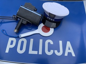 Na zdjęciu widoczna jest czapka policjanta Wydziału Ruchu Drogowego , urządzenie do pomiaru prędkości jak również tarcza policyjna do dawania sygnału do zatrzymania pojazdu tak zwany lizak