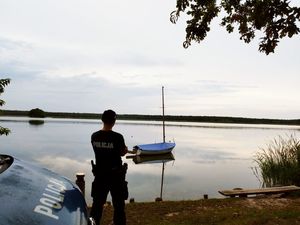 na zdjęciu widoczny jest zbiornik wodny , stojący umundurowany policjant oraz oznakowany radiowóz