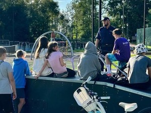 na zdjęciu widoczny jest umundurowany policjant rozmawiający z grupa dzieci na terenie skateparku w Boronowie