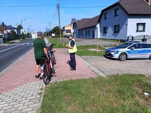 na zdjęciu widoczny jest oznakowany radiowóz , umundurowany policjant z ruchu drogowego , oraz rowerzyści stojący obok swoich rowerów .