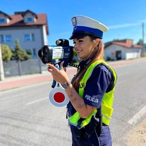 na zdjęciu widoczna jest policjantka w kamizelce odblaskowej trzymająca w ręce urządzenie pomiarowe prędkości.