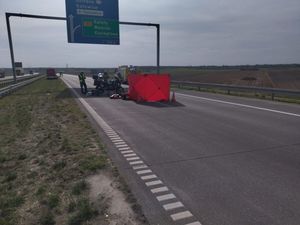 na zdjęciu widoczna jest autostrada na której stoją umundurowani policjanci  nad nimi widoczna jest duża tablica informacyjna widać również zasłonę stosowana podczas wypadków drogowych