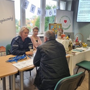 na zdjęciu widoczna jest umundurowana policjantka rozmawiająca ze starszym panem oboje siedzą przy stole