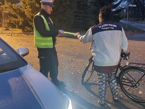 na zdjęciu widoczny jest oznakowany radiowóz oraz umundurowany policjant który wręcza rowerzyście odblask