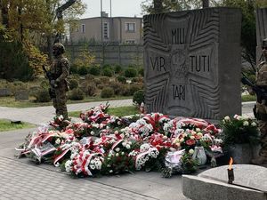na zdjęciu widoczny jest pomnik i złożone pod nim wiece obok stoi żołnierz