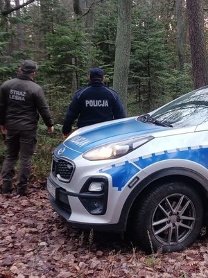 na zdjęciu widoczny jest oznakowany radiowóz oraz umundurowany policjant i strażnik leśny