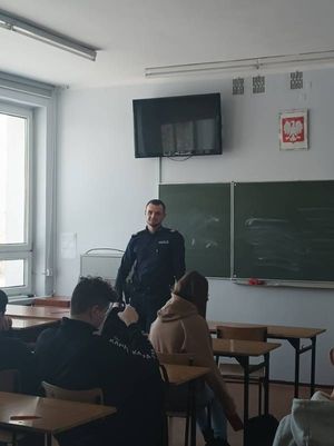 na zdjęciu widoczny jest policjant w umundurowaniu oraz siedząca młodzież w klasie