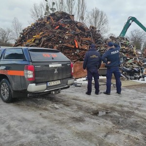 na zdjęciu widoczni są umundurowani funkcjonariusze STRAZY KOLEII I POLICJI STOJĄCY PRZY SAMOCHODZIE , A PRZED NIMI LEŻY DUŻY STOS ZŁOMU