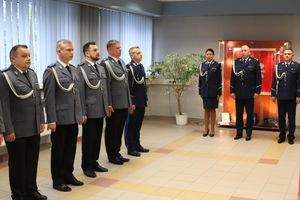 na zdjęciu widoczni są umundurowania policjanci części stoi w szeregu na wprost stoi dwóch umundurowanych komendantów i jedna umundurowana komendant