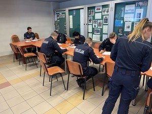 na zdjęciu widoczni są umundurowani policjanci siedzący przy stole i piszący