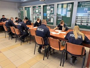 na zdjęciu widoczni są umundurowani policjanci siedzący przy stole i piszący