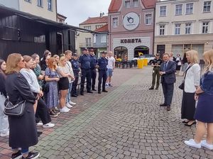 na zdjęciu widoczna jest młodzież stojąca a rynku i przemawiający do niej burmistrz miasta i wice burmistrz