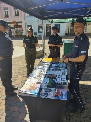 na zdjęciu widoczni są umundurowani policjanci stojący w namiocie i rozłożone na stole ulotki dot. handlu ludźmi