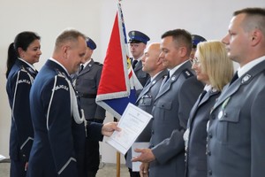 na zdjęciu widoczni są umundurowani policjanci stojący w rzędzie przed nimi stoi umundurowany policjant i policjantka policjant wręcza policjantowi akt nominacji na wyższy stopień