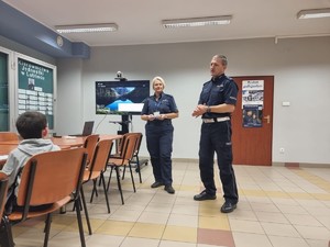 na zdjęciu widocznych jest dwoje umundurowanych policjantów stojanych na sali przed nimi duże stoły