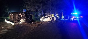 na zdjęciu widoczne są dwa przewrócone  pojazdy jeden na drodze drugi w rowie obok stoi dwóch umundurowanych policjantów oraz oznakowany radiowóz