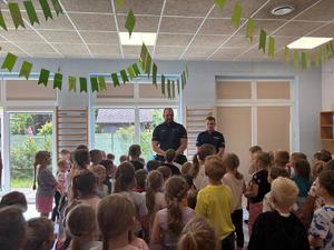 NA ZDJĘCIU WIDOCZNI SA DWAJ POLICJANCI ORAZ GRUP DZIECI PRZEDSZKONYCH