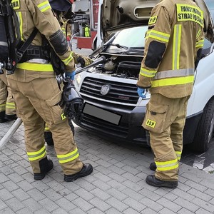 na zdjęciu widocznych jest dwóch umundurowanych strażaków stojących obok białego busa który ma podniesiona maskę