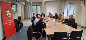 na zdjęciu widoczny jest stół wokół którego siedzą umundurowali strażacy i policjanci oraz osoby w cywilnych ubraniach