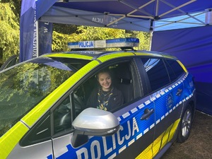 Na zdjęciu siedząca dziewczyna w oznakowanym radiowozie.