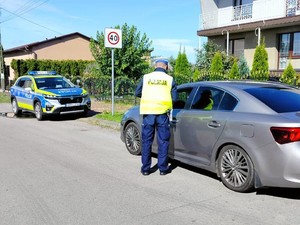 na zdjęciu widoczny jest umundurowany policjant stojący obok samochodu osobowego  jak również widoczny jest oznakowany radiowóz