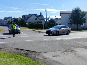 na zdjęciu widoczny jest umundurowany policjant który zatrzymuje samochód do kontroli