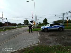 Na zdjęciu umundurowany policjant stojący obok przejazdu kolejowego.