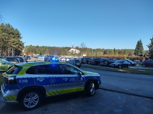 Na zdjęciu oznakowany radiowóz na tle cmentarza.