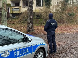 na zdjęciu widoczny jest umundurowany policjant stojący obok oznakowanego radiowozu na wprost  pustostanu