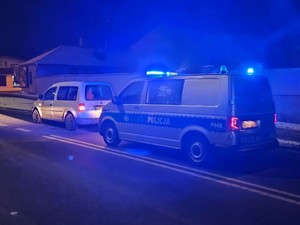 na zdjęciu widoczny  jest biały samochód za nim stoi oznakowany radiowóz pojazdy stoją na ulicy