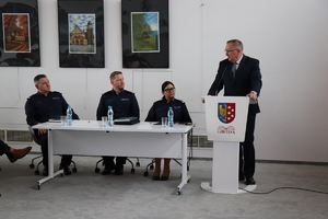 na zdjęciu widocznych jest troje umundurowanych policjantów siedzących przy stole obok przy mównicy stoi mężczyzna