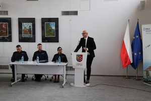 na zdjęciu widocznych jest troje umundurowanych policjantów siedzących przy stole obok przy mównicy stoi mężczyzna