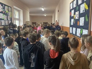na zdjęciu widoczne są dzieci stojące na korytarzu szkolnym wśród nich widoczny jest umundurowany policjant