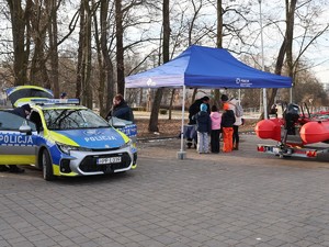na zdjęciu widoczny jest radiowóz policyjny oraz namiot policyjny obok namiotu stoją dzieci i umundurowani policjanci
