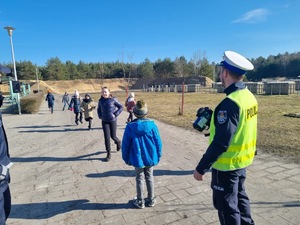 Na zdjęciu umundurowany policjant Wydziału Ruchu Drogowego stojący z urządzeniem do pomiaru prędkości.
