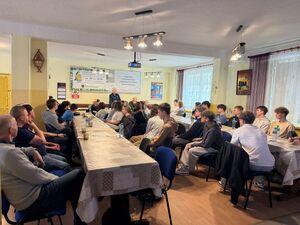 za stołami siedzą młodzi ludzie przed nimi stoi policjantka